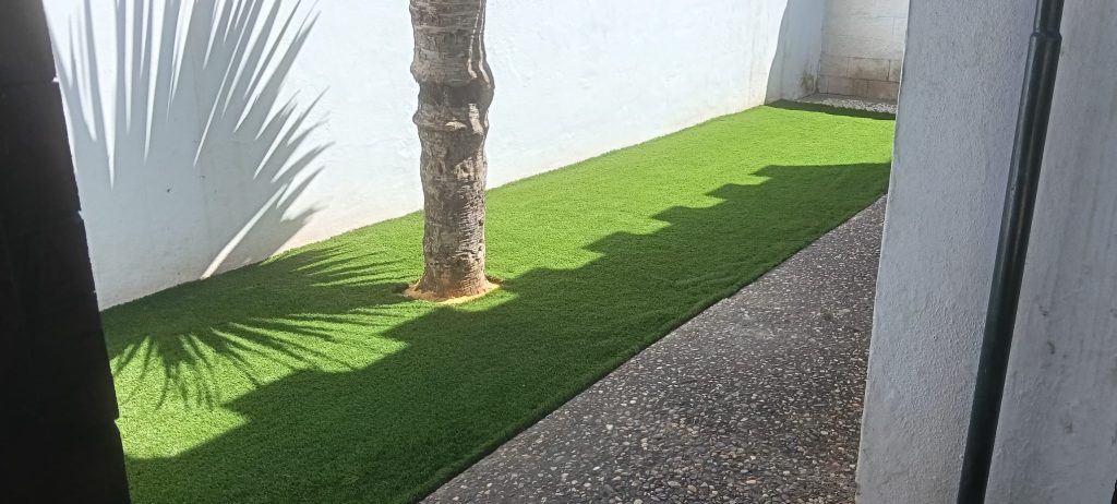 Instalación de césped artificial terminada junto a palmera - Limcesped Sevilla
